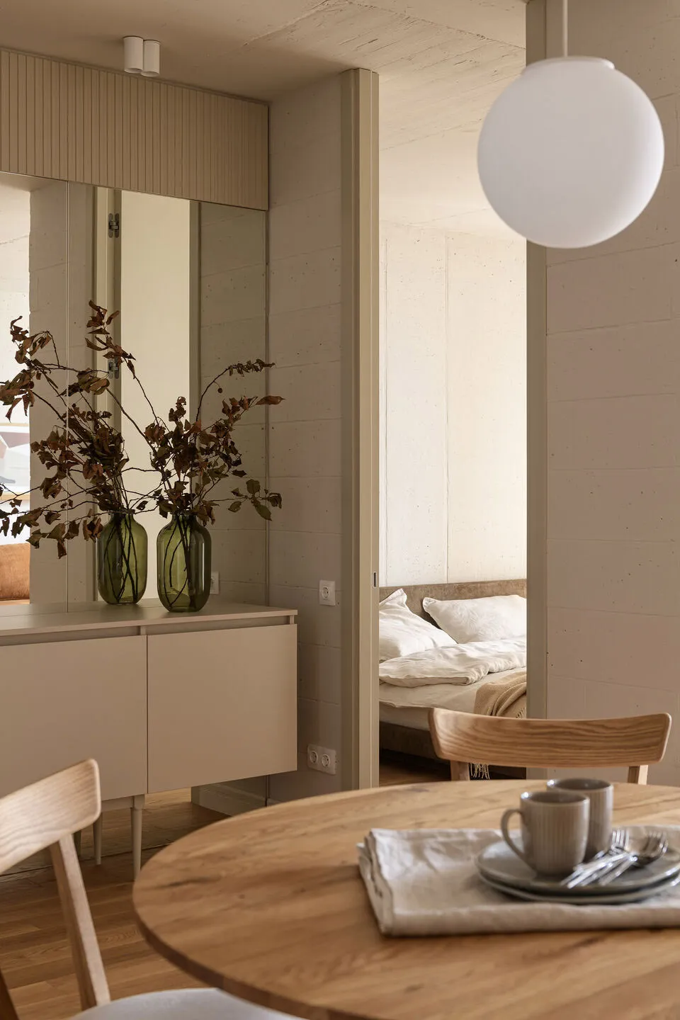 Modern minimalist residential interior featuring wooden table, concrete walls, and glass vase with dried leaves.