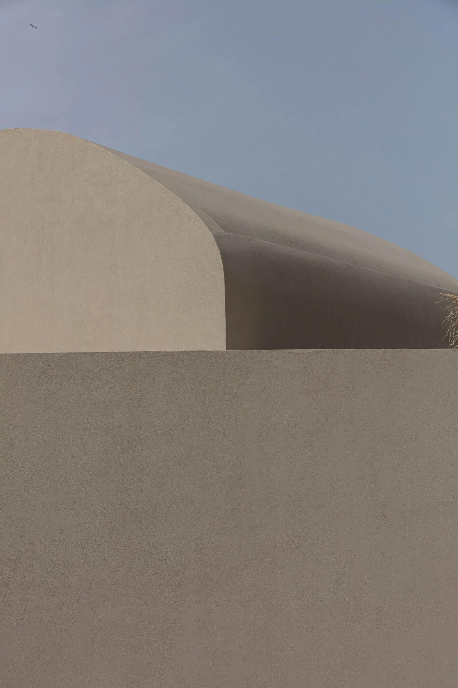 A minimalist sand hill with smooth, curved surfaces under a clear blue sky.