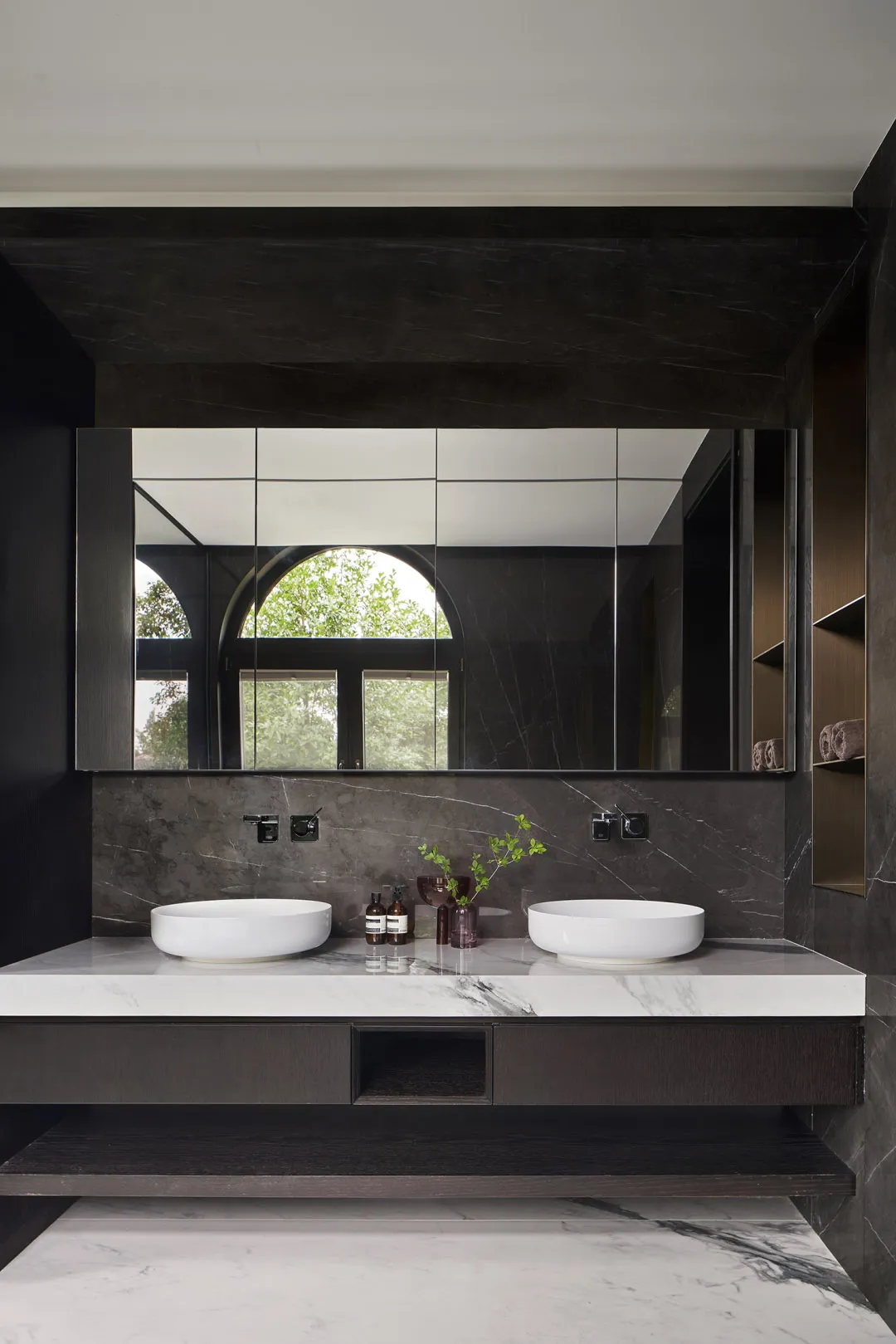 A modern bathroom with a marble countertop and vanity, featuring a large mirror and a window with green trees outside.