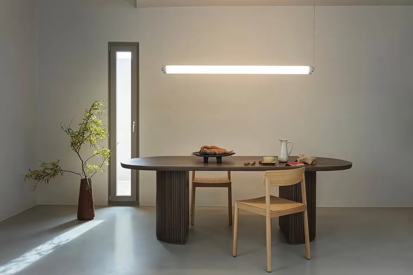 一間現代餐廳,擺放著簡約設計的木質餐桌,搭配餐椅與花瓶植物,搭配落地燈。