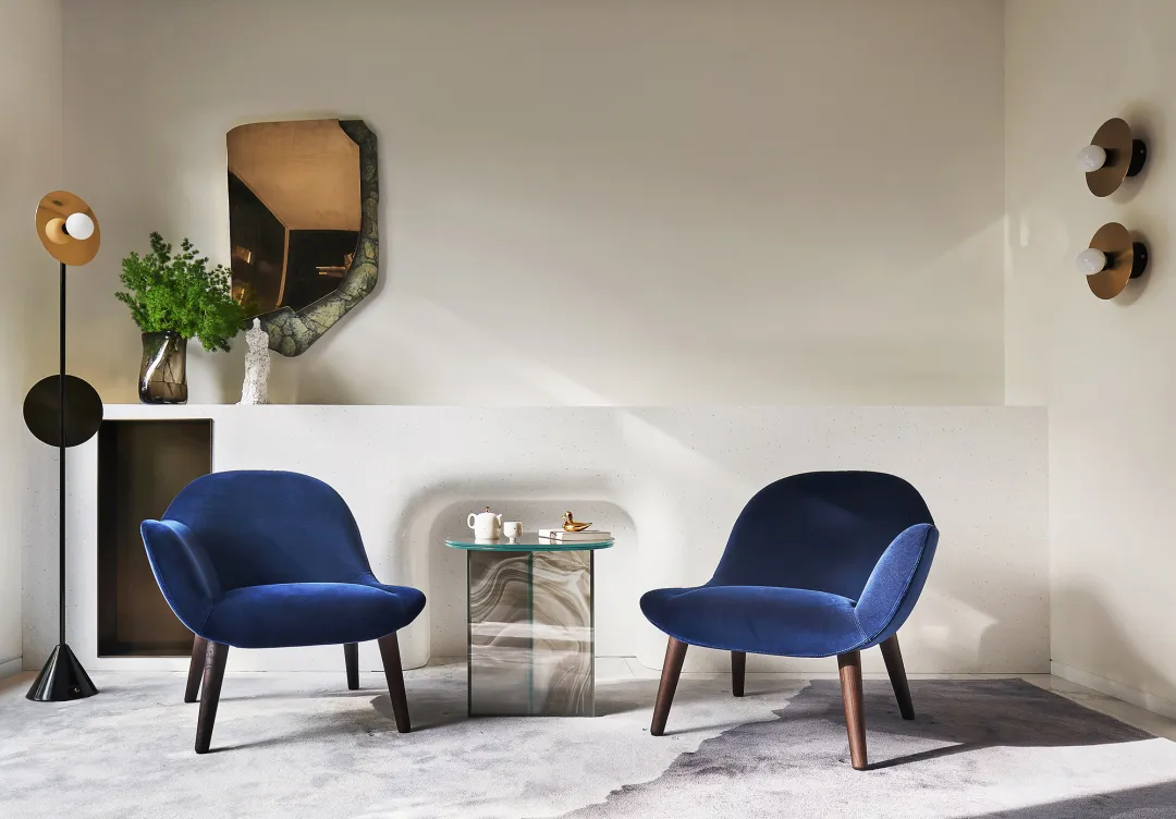 A modern living room with two blue velvet armchairs, a marble side table, and a minimalist decor style.