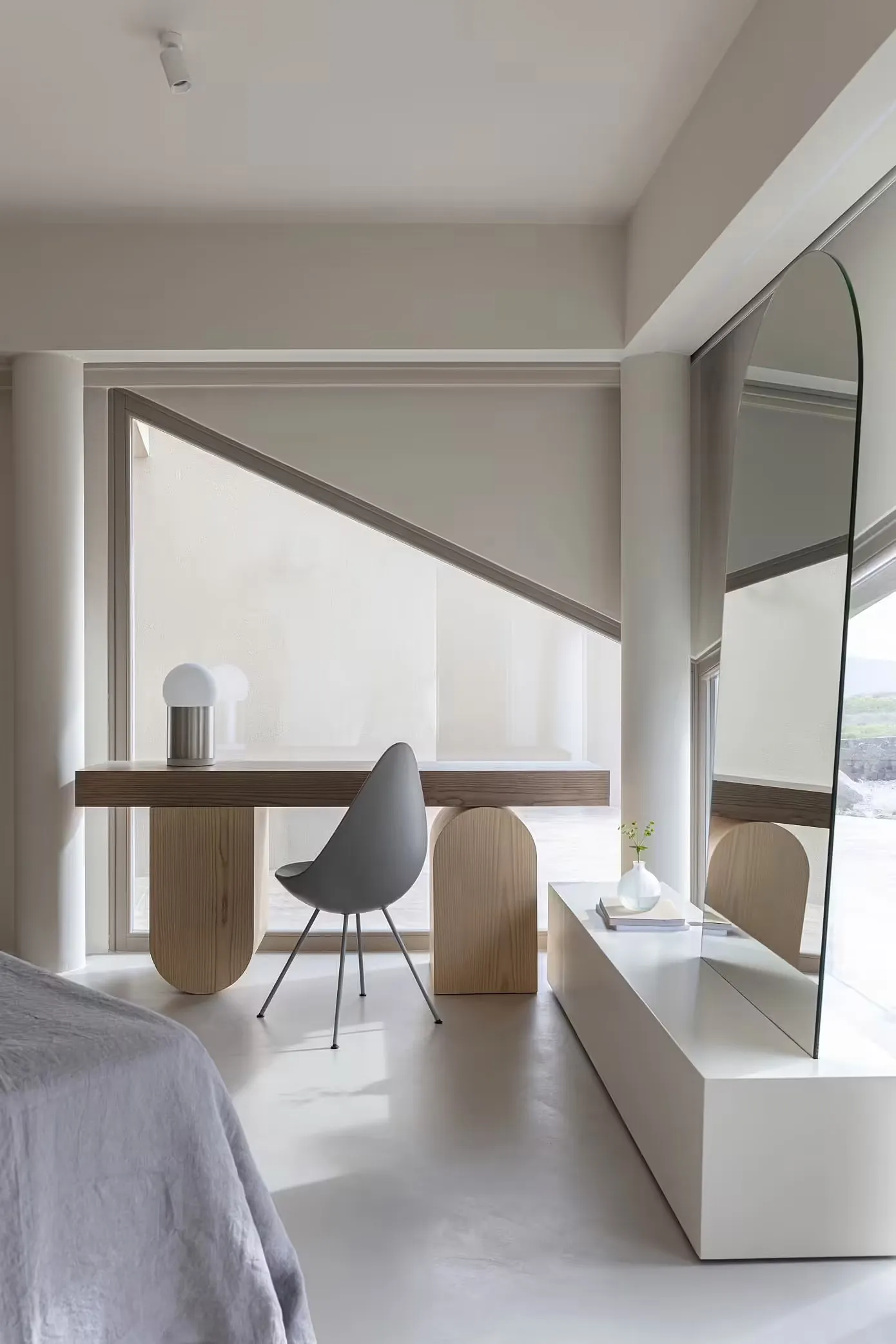 A modern minimalist bedroom featuring a wooden desk, gray chair, and glass table.