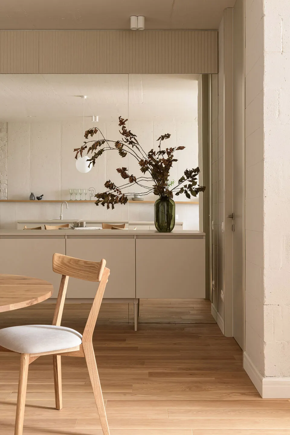 Modern minimalist kitchen interior with wood accents and a vase of dried branches.