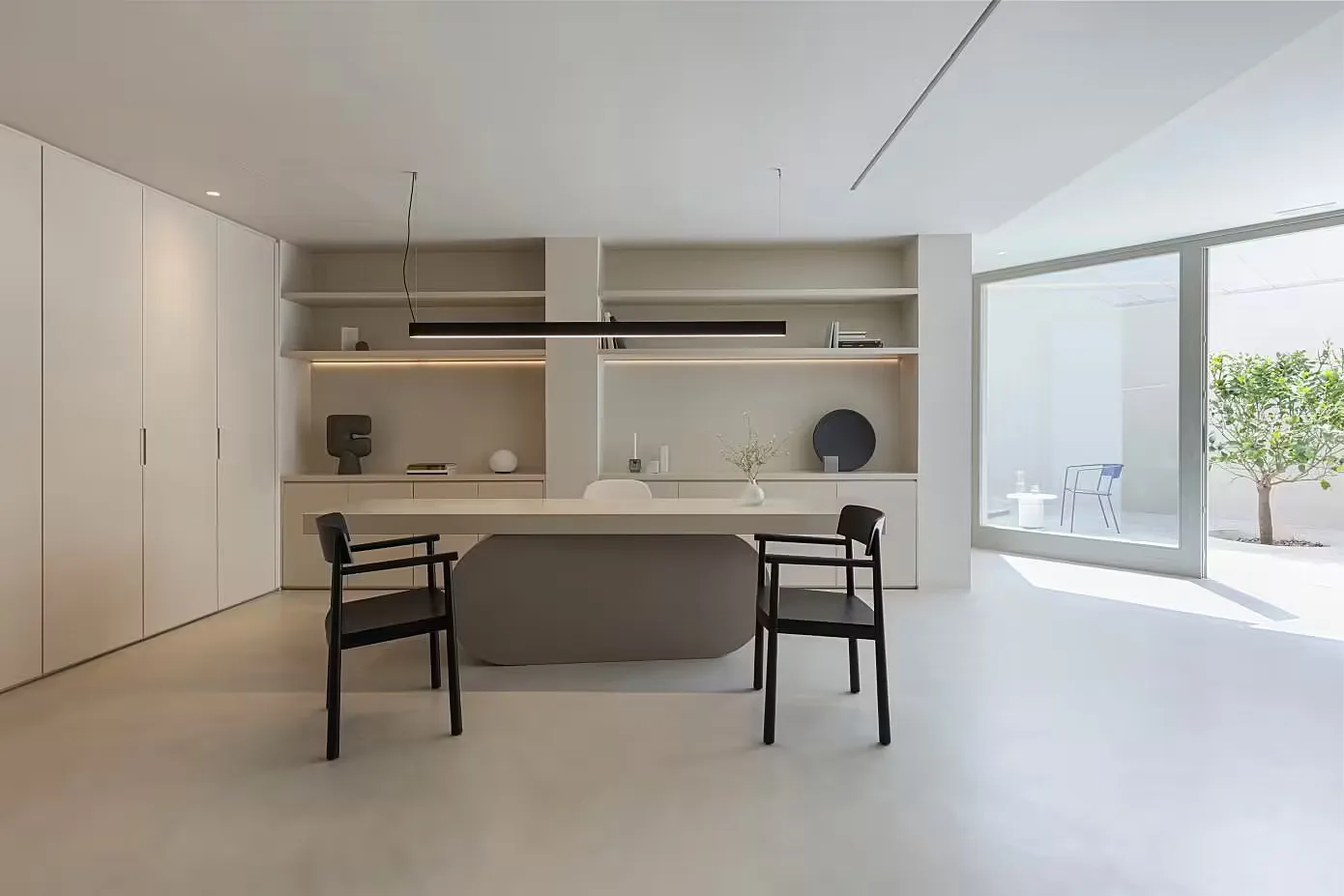A modern minimalist office with a concrete desk, black chairs, and a sleek, white storage unit with built-in shelves.