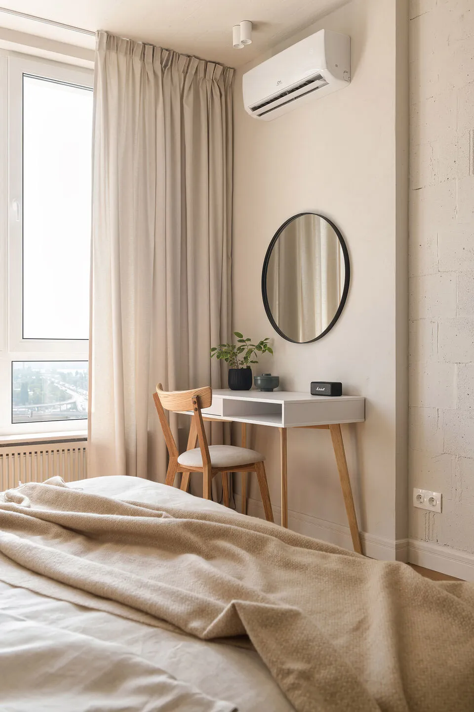 一間極簡風格的臥室,採用中性色調,配有米色床罩的床、一張帶圓形鏡子的書桌,以及米色窗簾