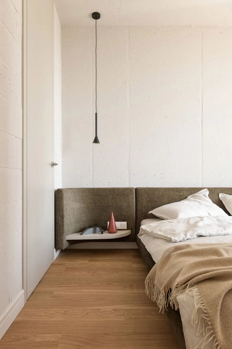 Modern bedroom featuring a concrete headboard bed with minimalist decor and wooden flooring.