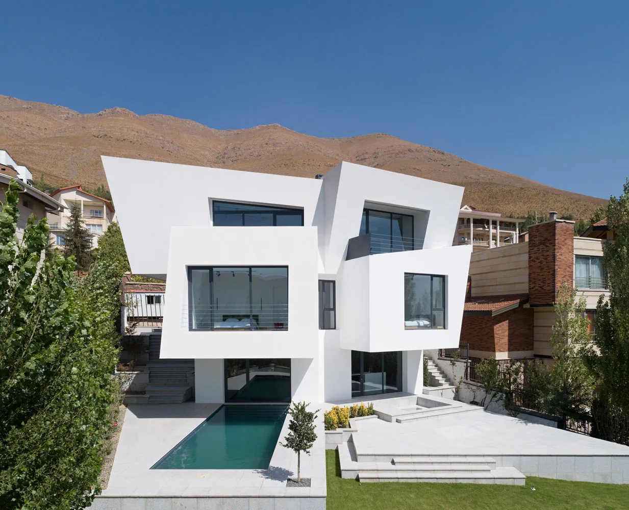 Modern minimalist house with white concrete walls, large glass windows, and a landscaped yard.