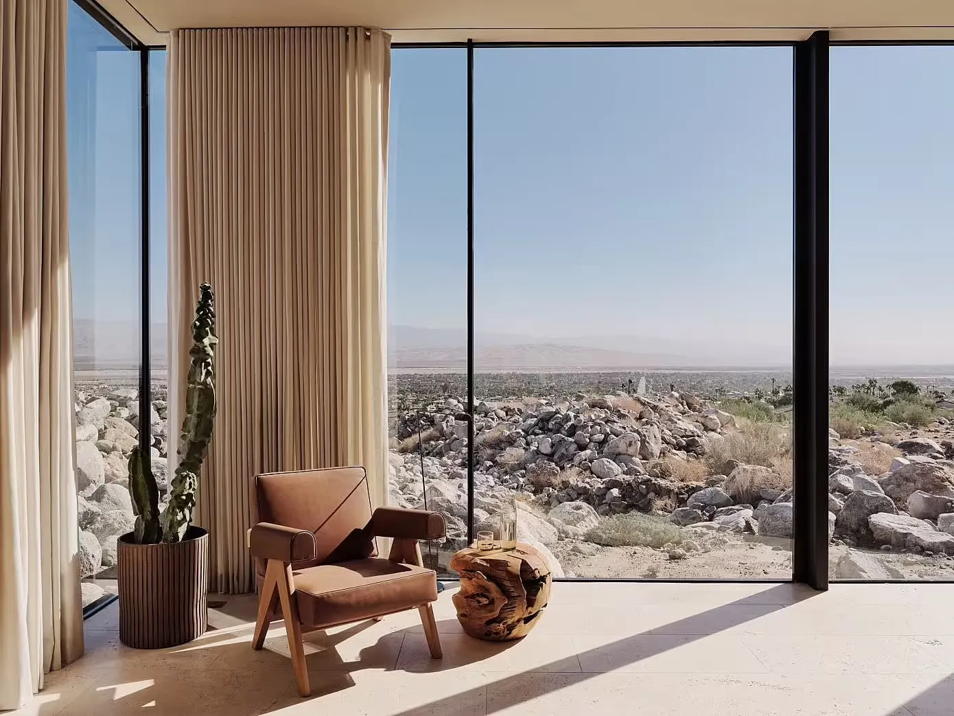 A minimalist living room with a wooden armchair and a cactus plant in a pot.
