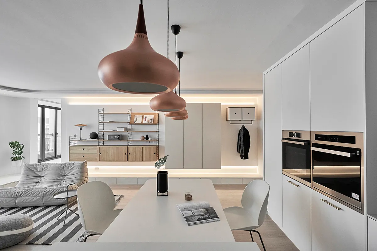 A modern, minimalist kitchen and dining area featuring white cabinets and a white table with a geometric pendant light fixtur