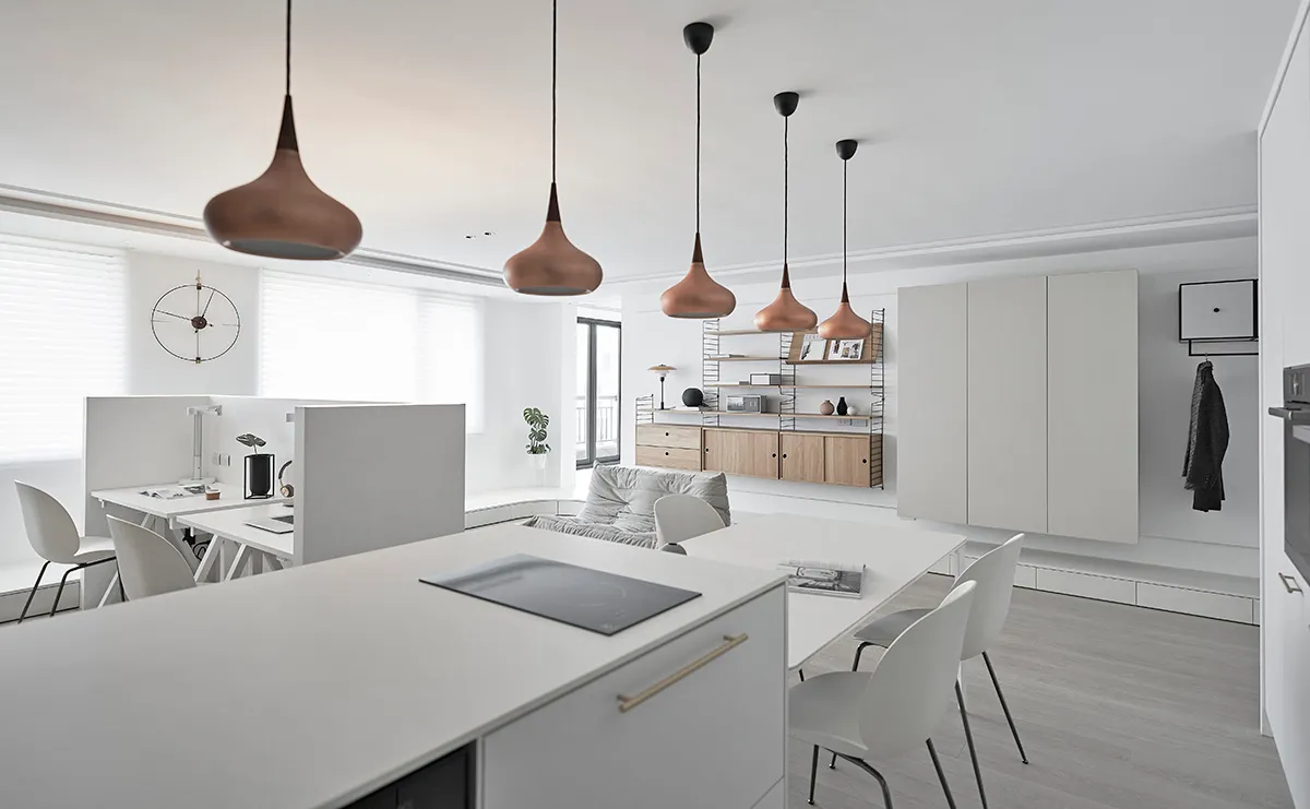 A modern office kitchen with white materials and minimalist design, featuring a white countertop, pendant lights, and a white