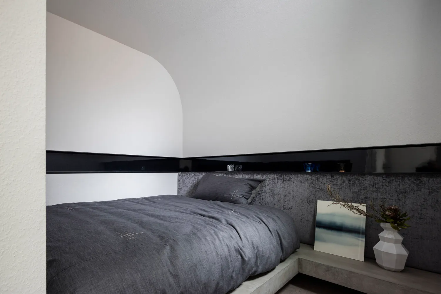 A modern minimalist bedroom with a grey upholstered bed on a concrete platform, illuminated by soft light and accented with a