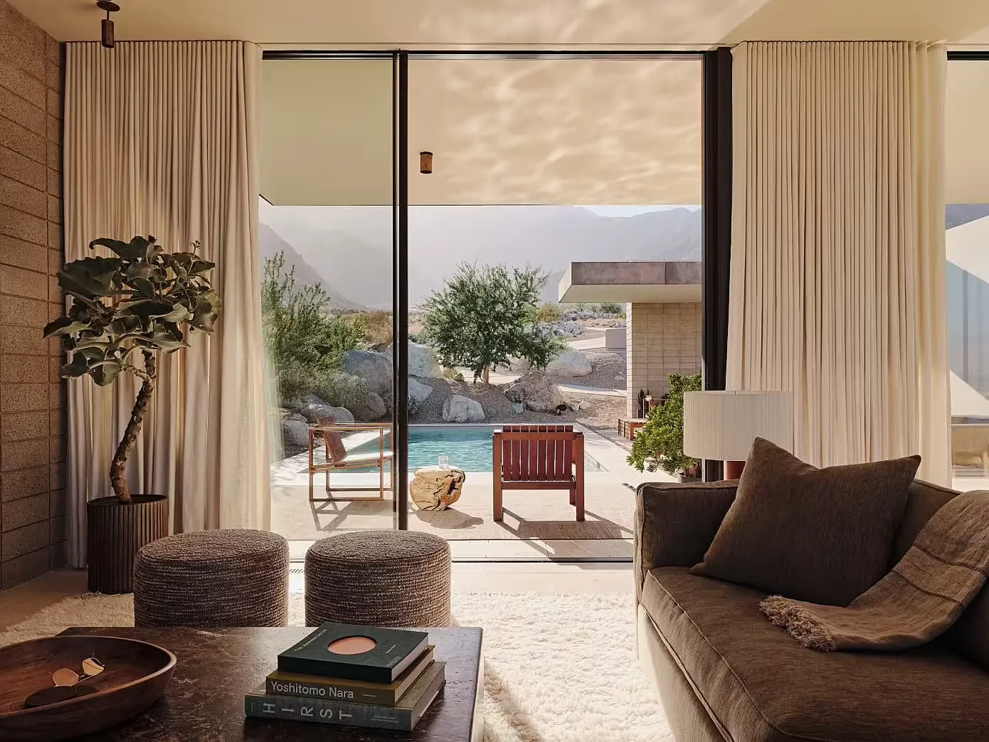 A modern minimalist living room with a large window, a comfortable sofa, and a view of a pool and mountains.