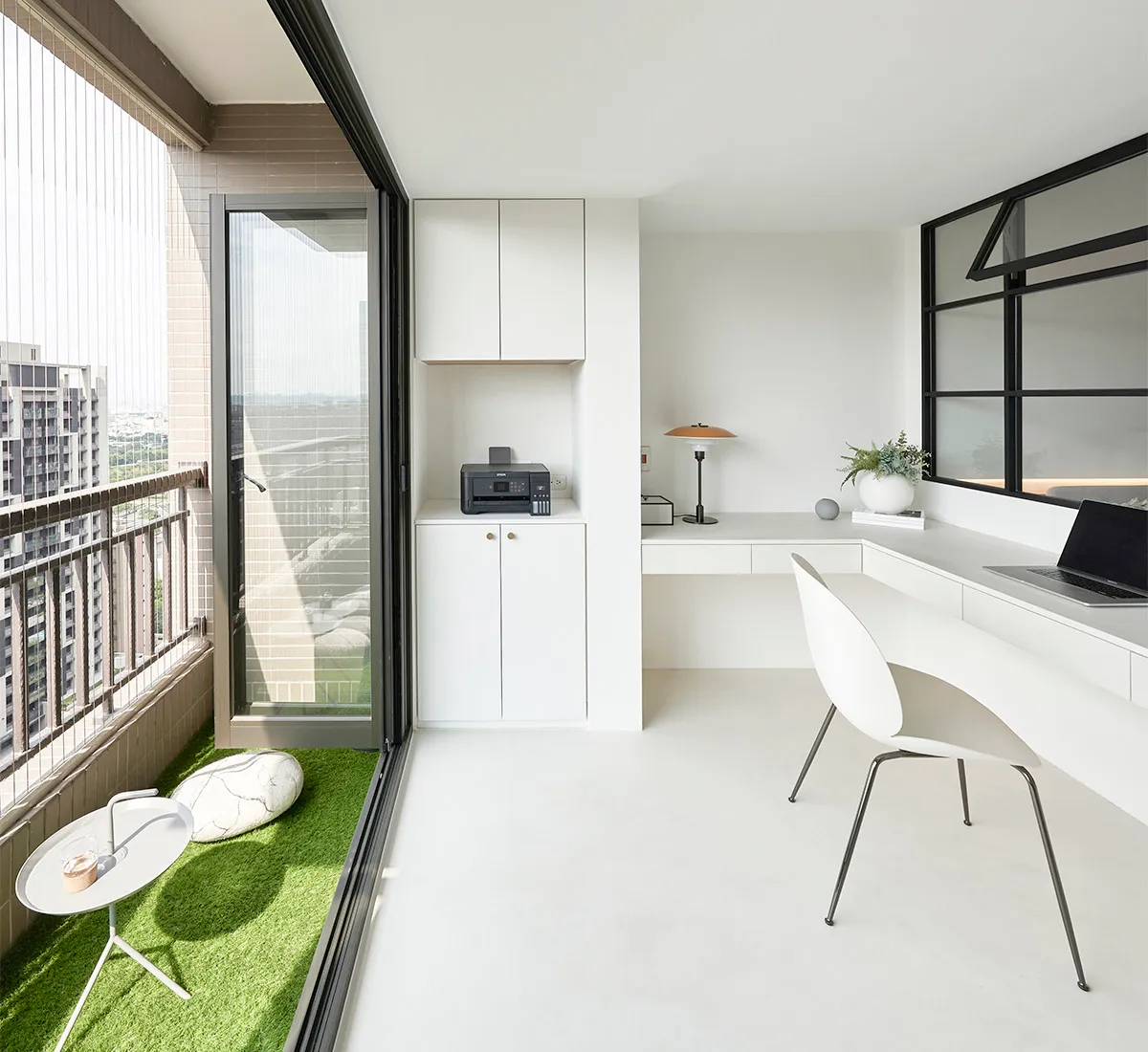 A minimalist office with white furniture, a large window, and green accents on the floor.