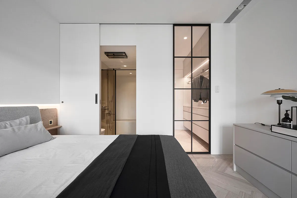 Modern minimalist bedroom with white walls, a bed, and a sliding glass door leading to a closet.