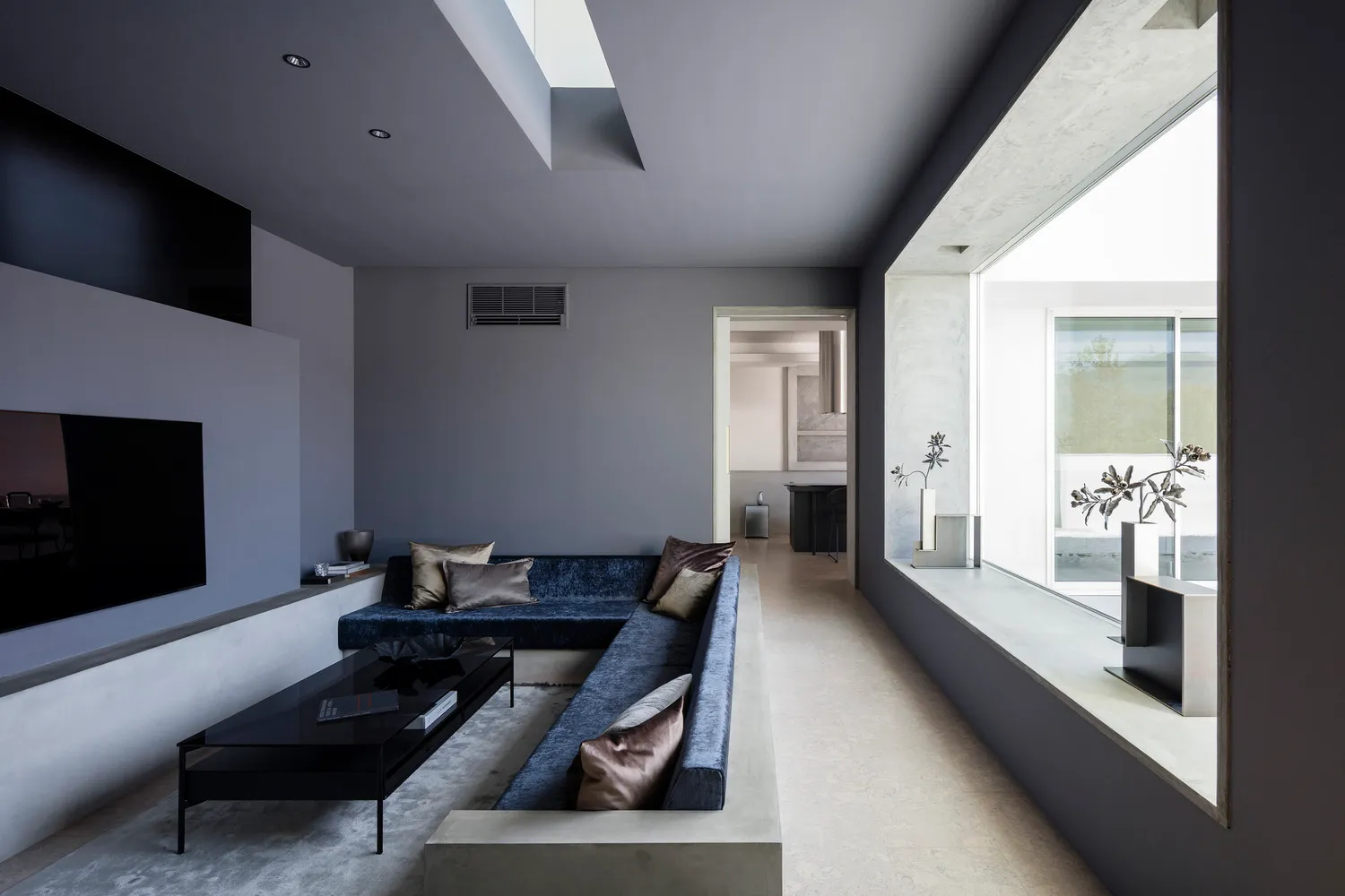 A minimalist living room with a concrete interior, featuring a sleek blue sofa and a flat-screen TV.
