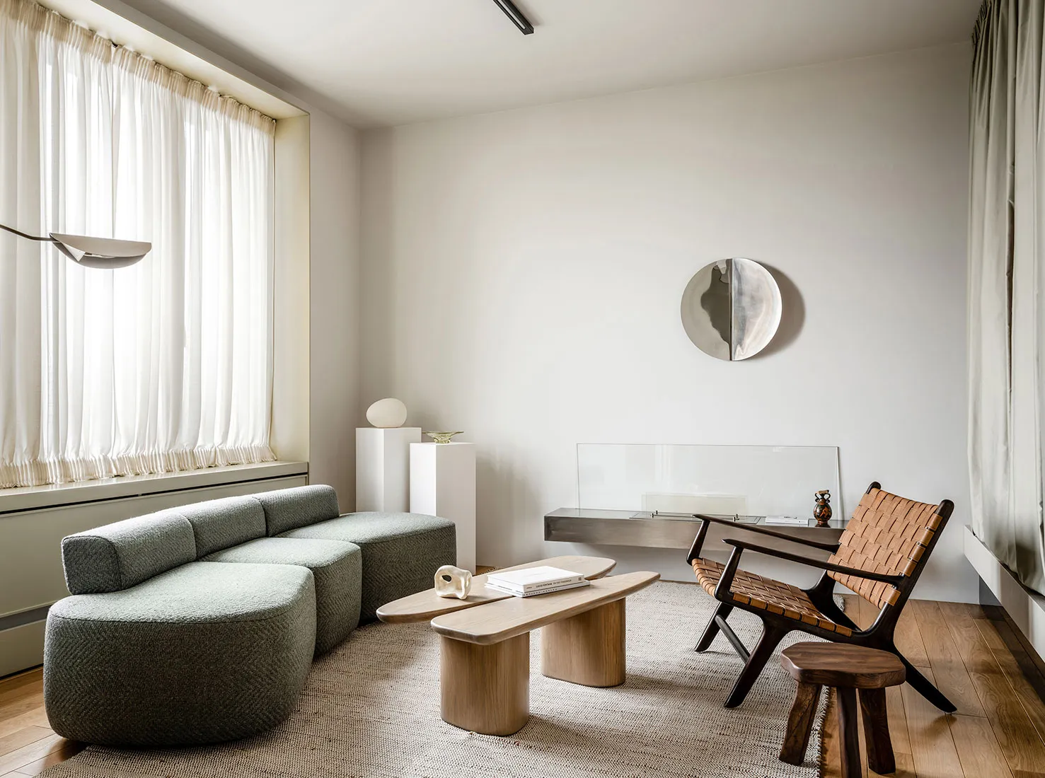 A modern minimalist living room featuring a gray upholstered sofa, wooden side tables, and glass wall decor.