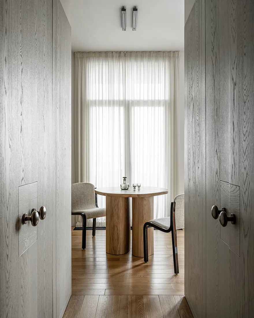 Modern dining room with wooden table and chairs, minimalist design, and large window for natural light.