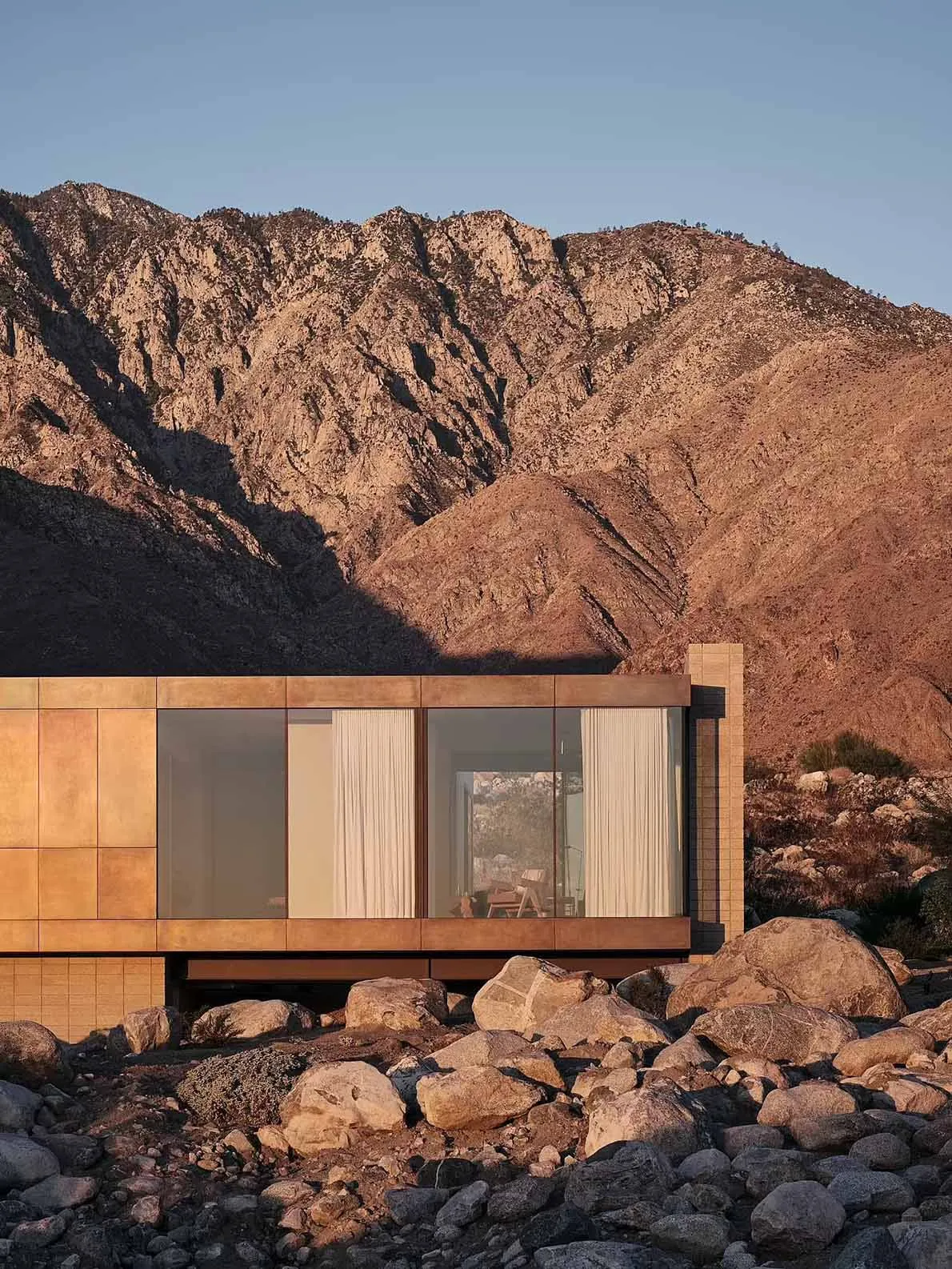 Modern residential house with metal-clad exterior and large glass windows against a mountainous backdrop.