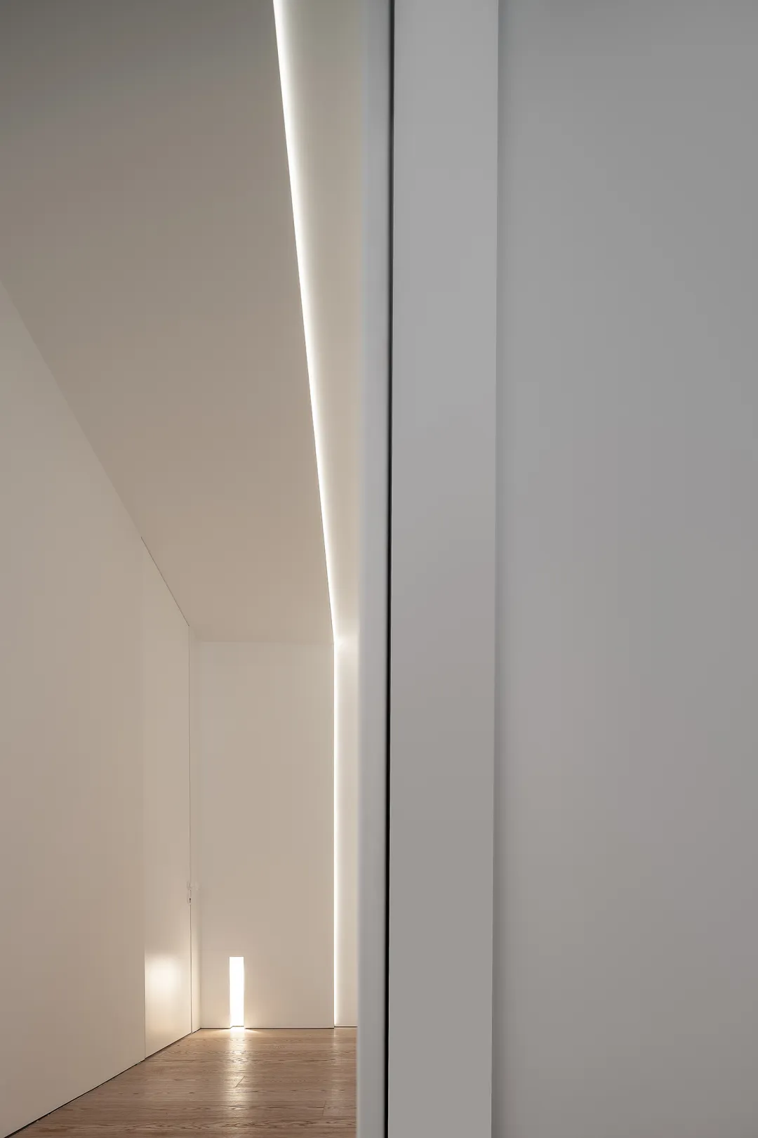 A minimalist interior space with white walls, floor-to-ceiling lighting, and wood flooring.