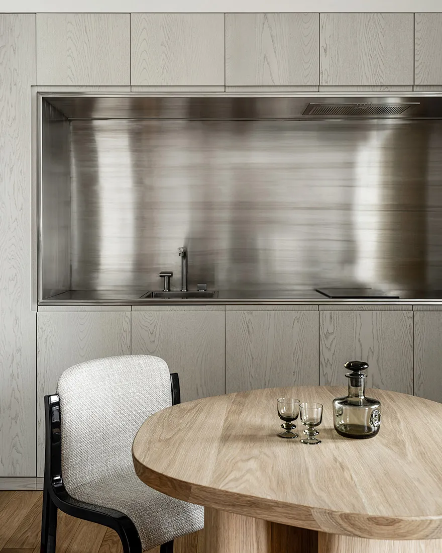 A minimalist modern kitchen with metallic finishes and a round wooden table.