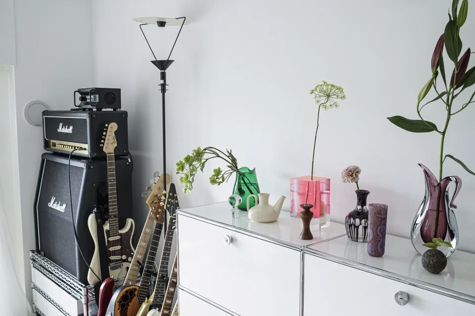 Minimalist music room featuring guitars, Marshall amplifiers, and decorative vases on a white cabinet.