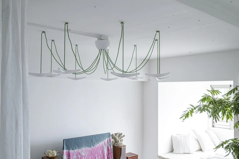 A modern, industrial-style living room with exposed concrete ceiling, a chandelier with green, hanging cables, and a white so