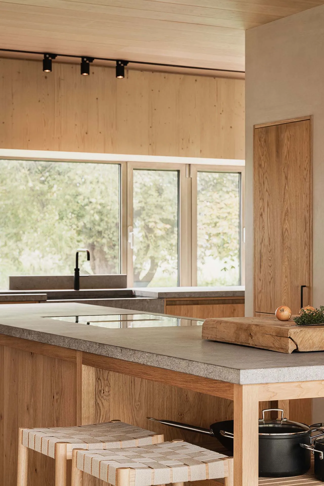 A modern kitchen interior with a concrete countertop and wooden stools.