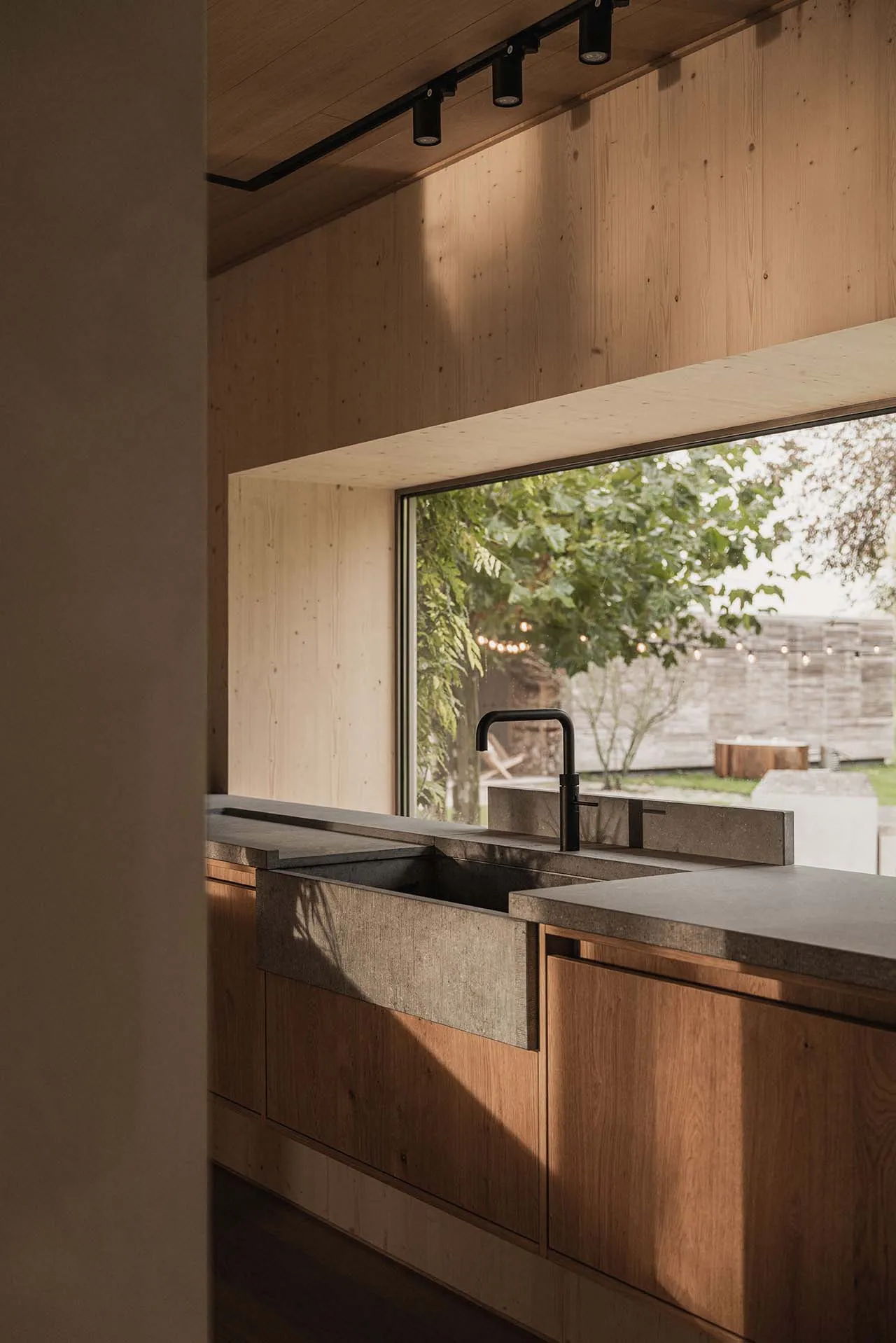 Modern kitchen with concrete sink, wooden cabinetry, and large window overlooking greenery.