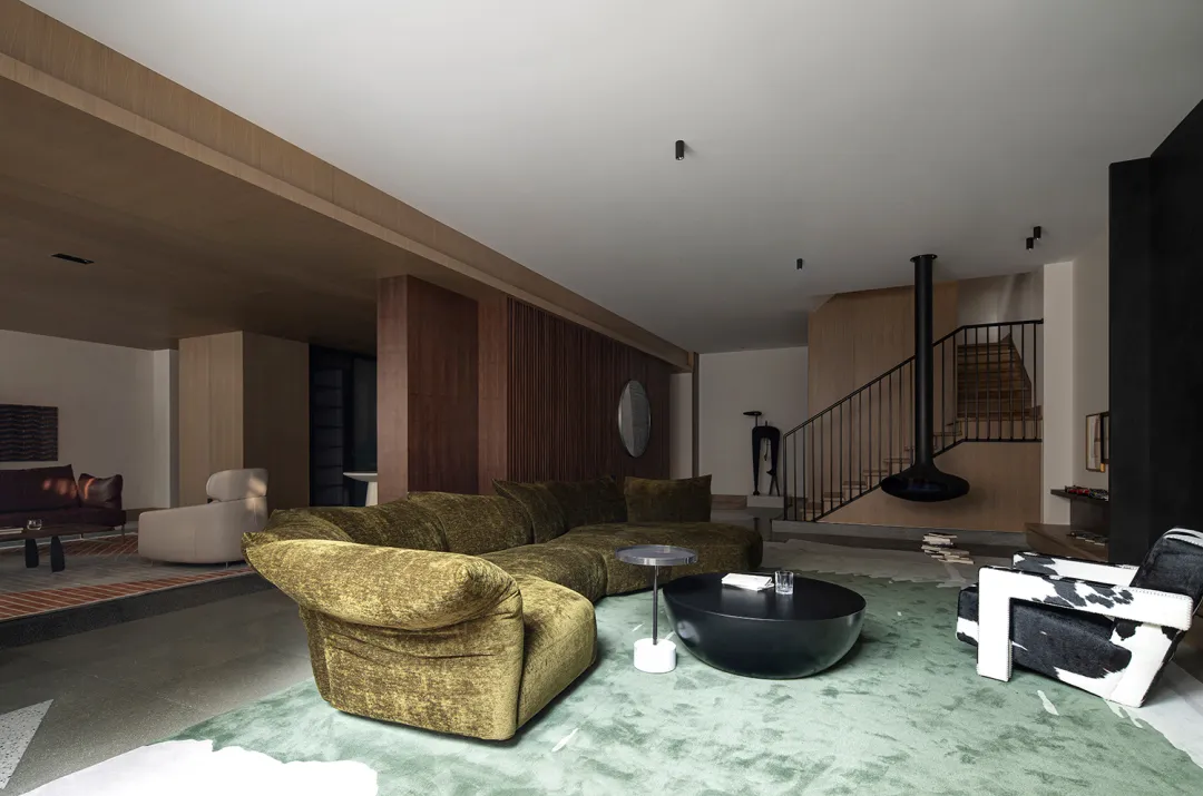 A modern minimalist living room featuring a large green upholstered couch, a black coffee table, and a black hanging fireplac