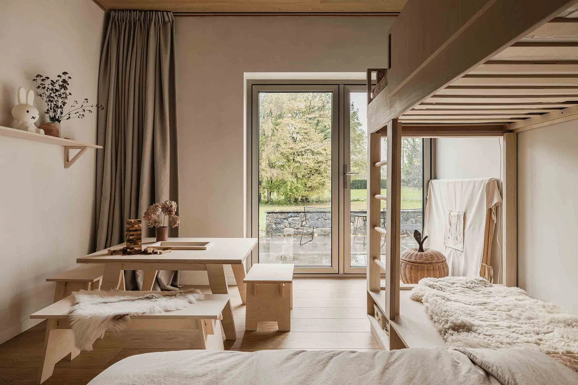 Minimalist bedroom with wooden furniture and a window overlooking a garden.