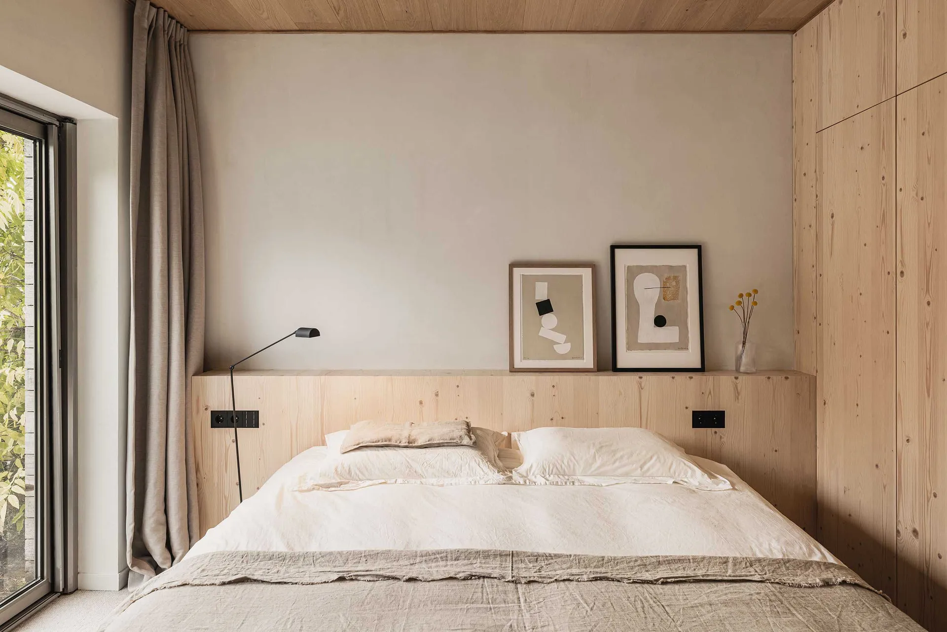 A modern minimalist bedroom with a wooden headboard and abstract art.
