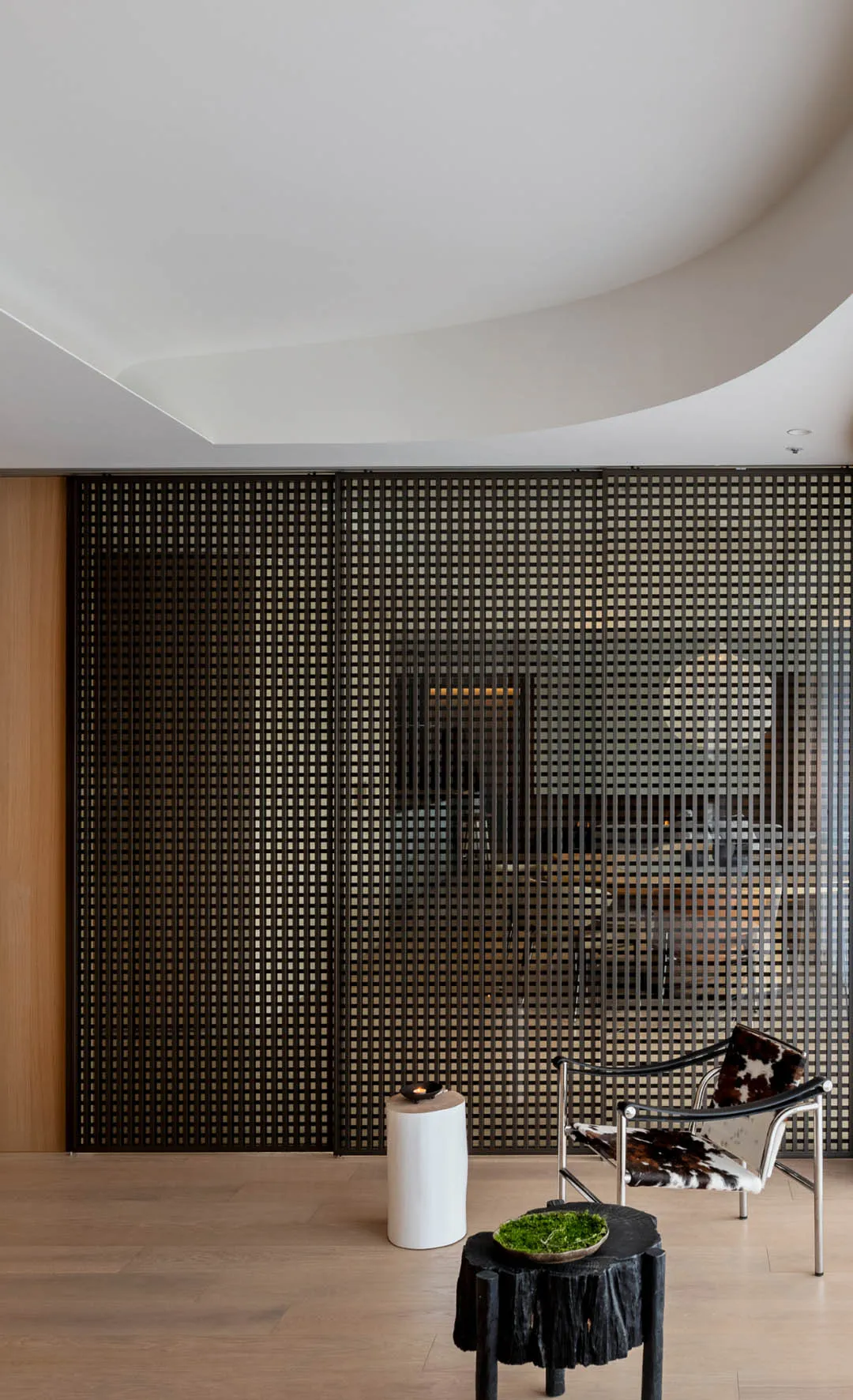 Modern minimalist living room featuring a black grid partition, wooden floor, and a single black and white cowhide chair.
