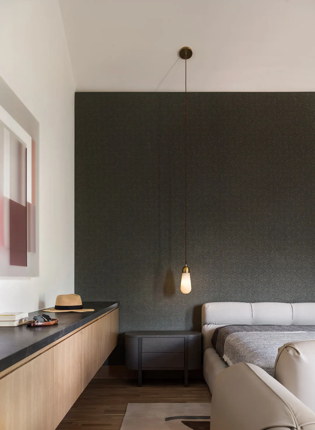 Minimalist bedroom featuring a textured gray wall, hanging light fixture, and neutral-colored furniture.