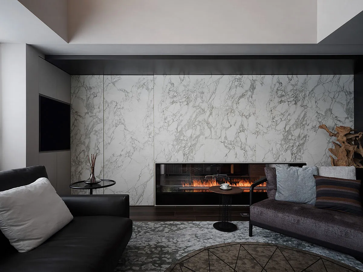 A modern living room featuring a large marble wall with a built-in fireplace, a black leather sofa, and a dark wood coffee ta