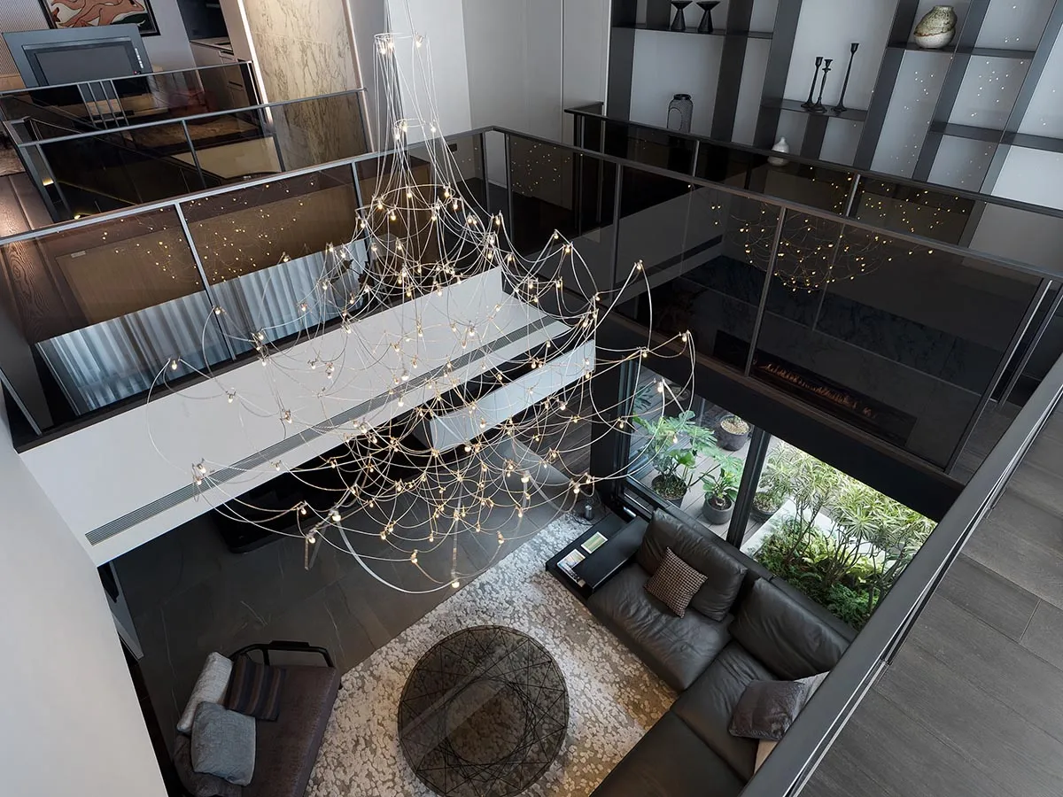Modern living room with a glass and metal chandelier, a leather sofa, and a circular glass table.