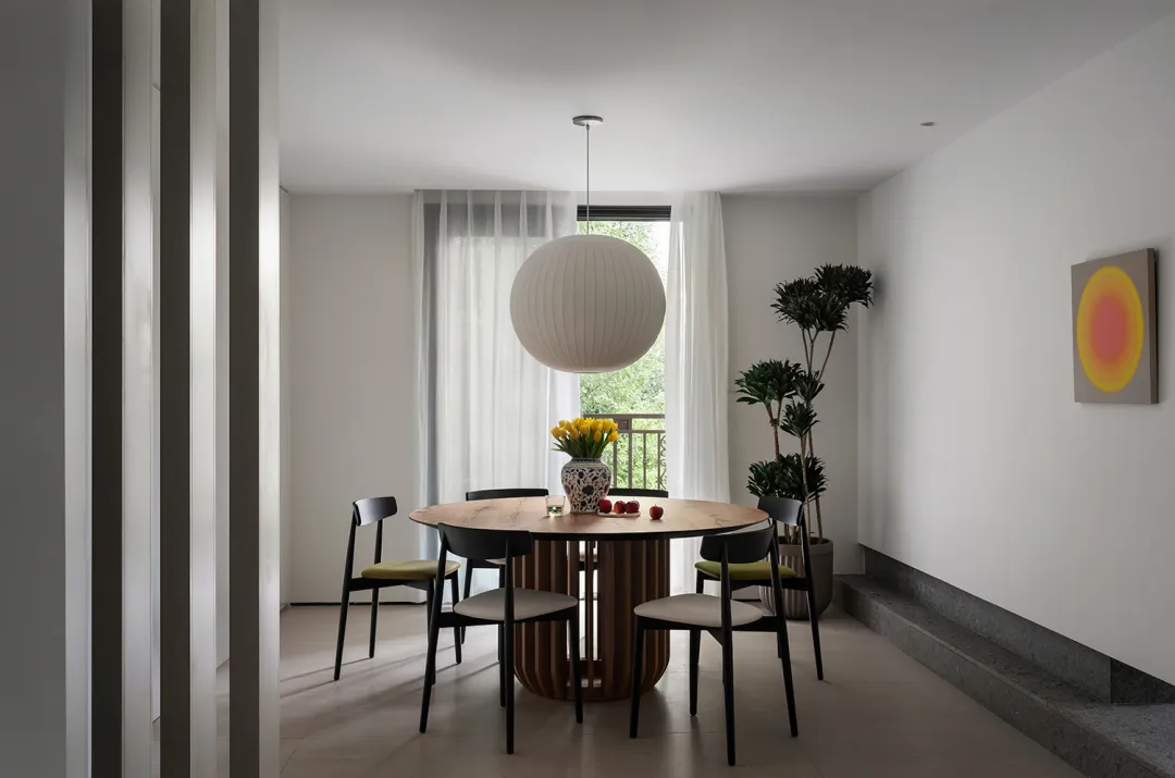 Modern, minimalist dining room featuring a round wooden table surrounded by black chairs, with a round pendant light, yellow