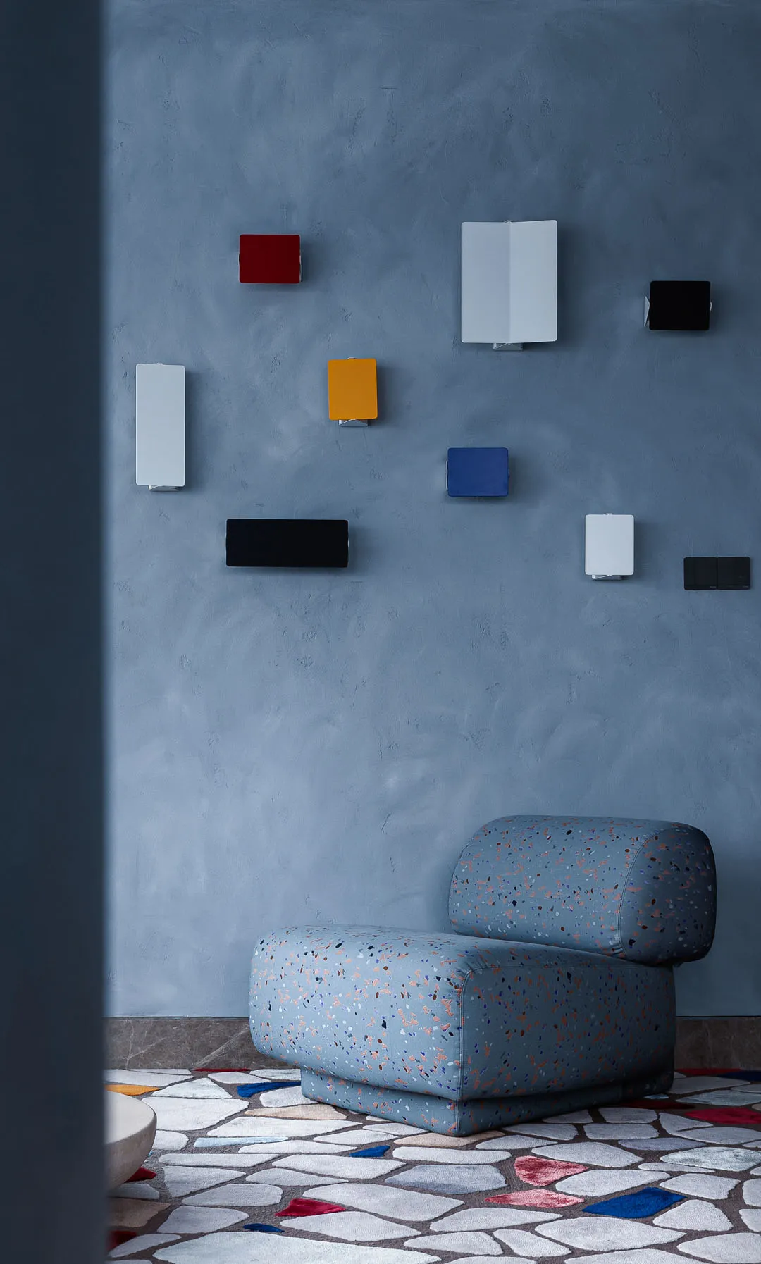 A minimalist living room with terrazzo flooring, featuring a modern, comfortable chair and colorful wall art.