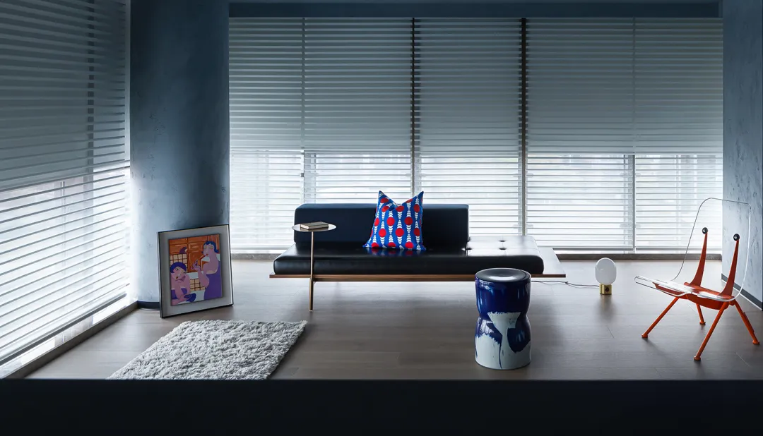 A modern living room with a concrete floor, wooden furniture, and horizontal blinds on the windows.