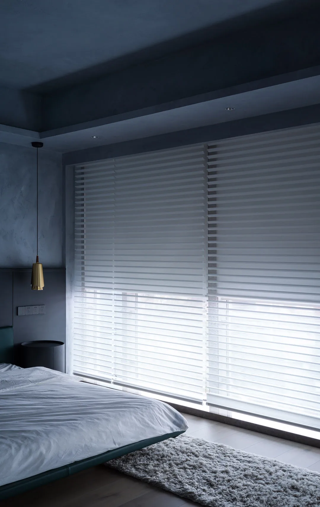 A modern minimalist bedroom with silk blinds, a cozy rug, and a sleek bed.