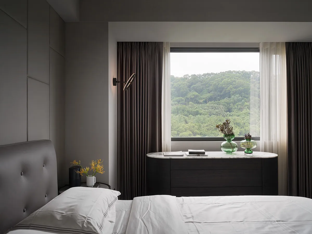 A modern minimalist bedroom featuring textured curtains, marble furniture, and a large window overlooking lush greenery.