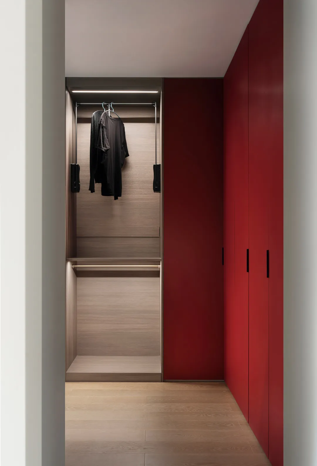 A modern minimalist closet with light brown wooden doors and shelves, featuring two black shirts hanging on a rail.