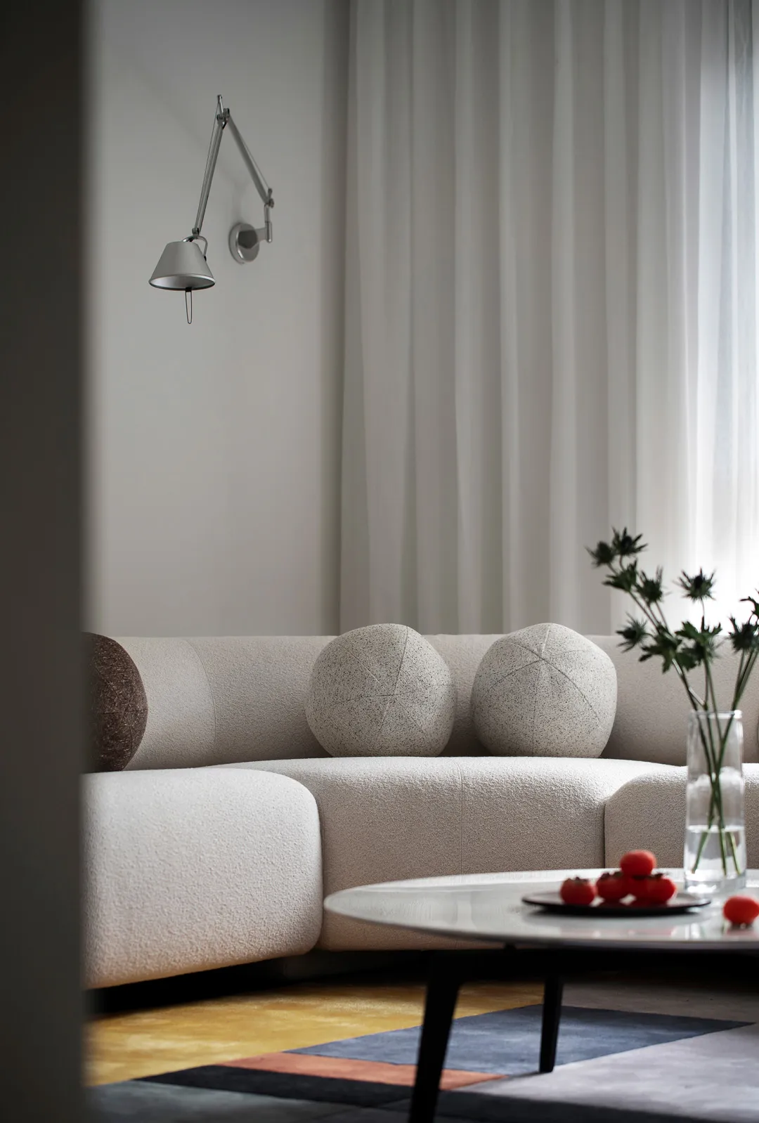 A modern white living room with textured fabric sofa, spherical throw pillows, round coffee table, and minimalist decor.