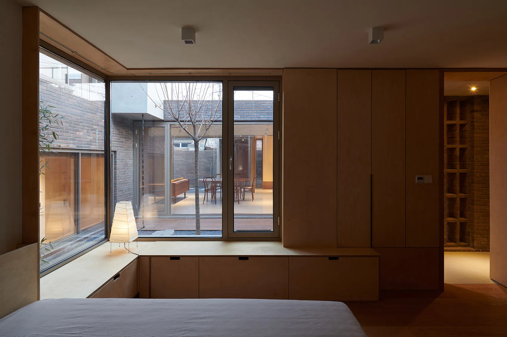 A minimalist bedroom with wooden cabinets and a large window overlooking a courtyard.