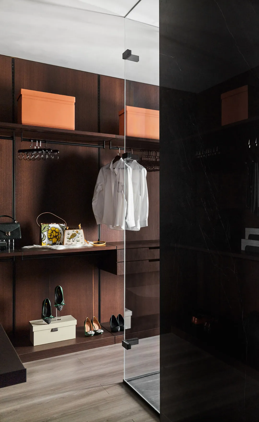 A modern minimalist wooden closet with sleek black marble accents, featuring a white shirt hanging, black and white bags, and