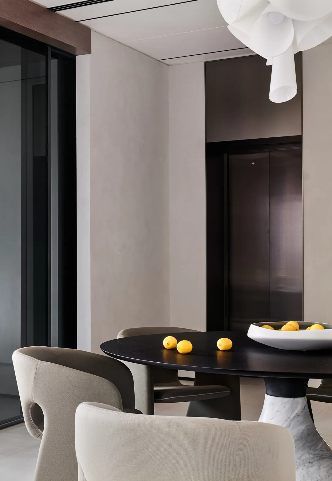 A minimalist residential dining area featuring a black table with a bowl of lemons and a white marble base.