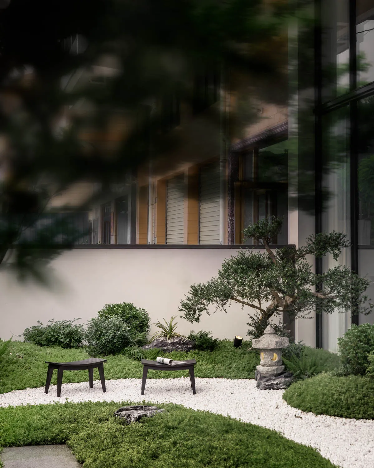 A minimalist Japanese garden featuring concrete, gravel, and greenery.