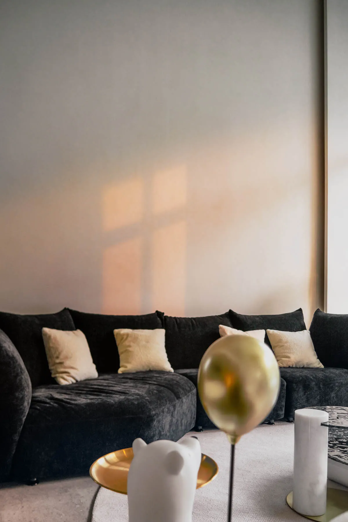 A modern minimalistic living room featuring a black velvet sofa with white cushions, a gold metallic balloon, and a white cer