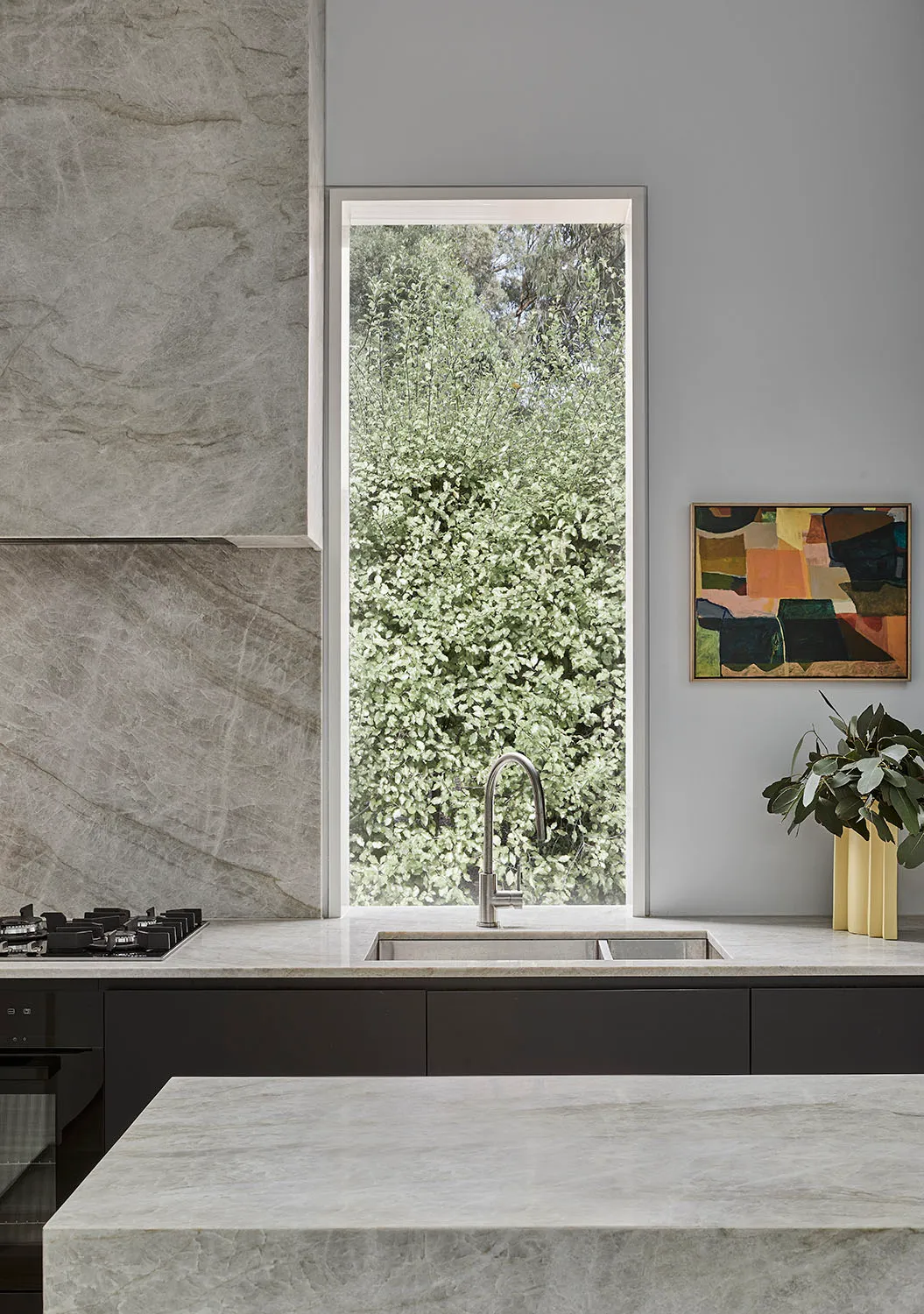 A modern kitchen with marble countertops and a large window overlooking greenery.