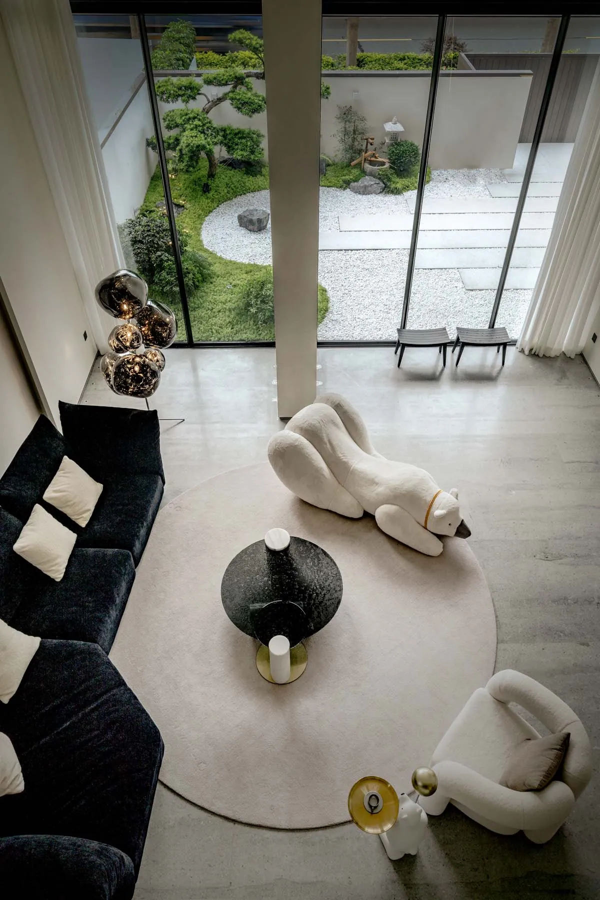 A modern living room featuring a minimalist design with concrete flooring, black sofas, and a white polar bear sculpture on a
