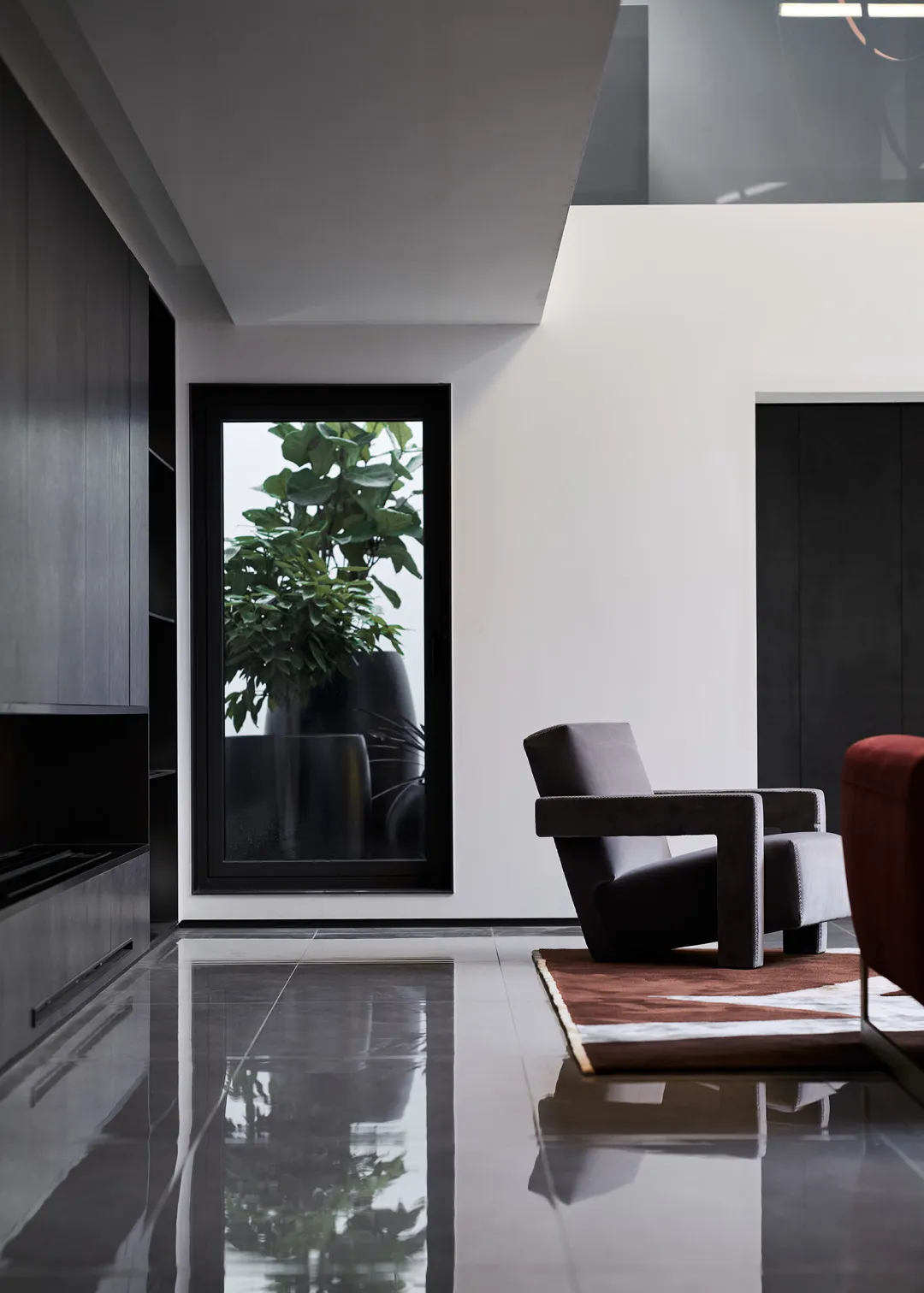 A minimalist modern living room with a sleek dark armchair, a rug, and sleek dark wooden cabinetry with a tall window display